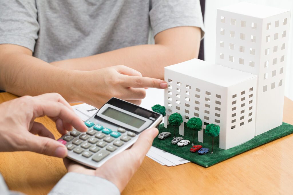 Pessoa calculando taxa condominial com maquete de condomínio atrás